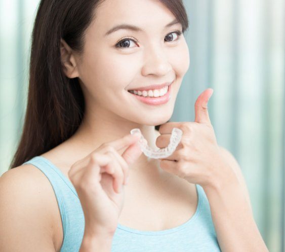 Woman holding Invisalign tray and giving a thumbs ups