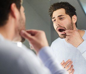 Man with lost dental crown looking at his smile in the mirror