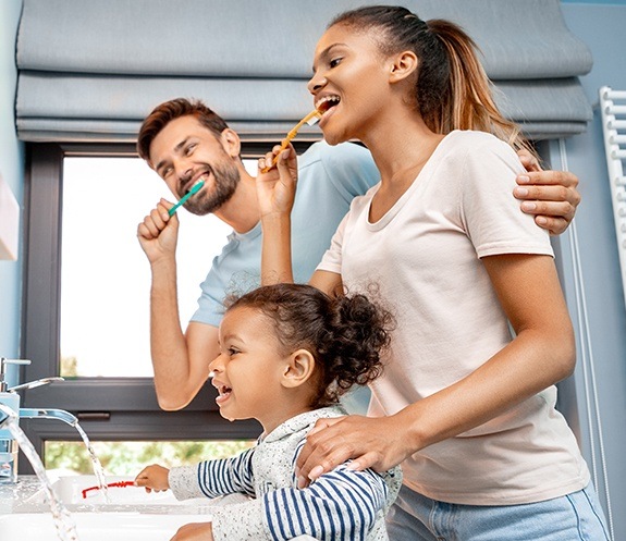 Family of three brushing teeth together to prevent dental emergencies