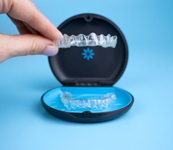 Fingers lifting Invisalign tray out of its case with blue background