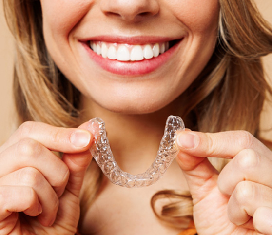 Nose-to-chest view of woman smiling holding clear aligner