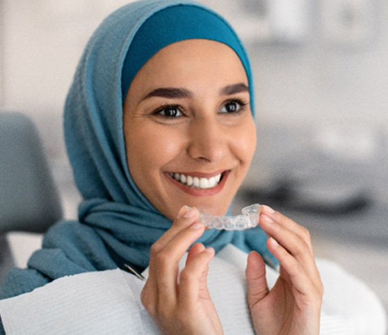 Woman in blue head covering in dental chair holding Invisalign