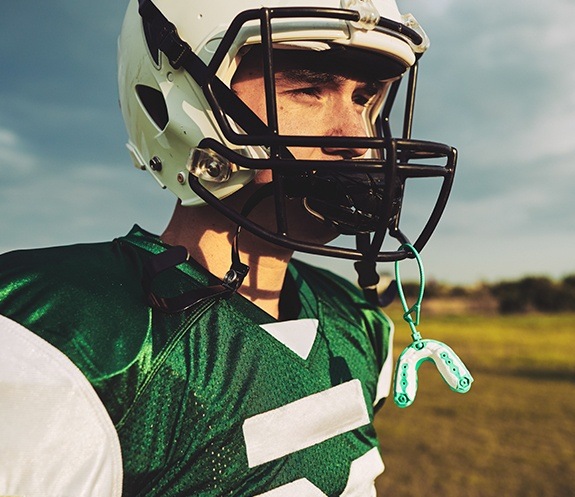 Teen in football gear with athletic mouthguard attached to helmet