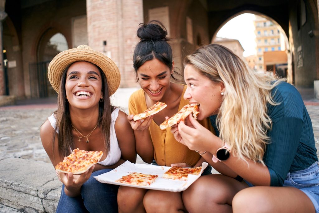 Group of friends smiling while eating pizza on vacation
